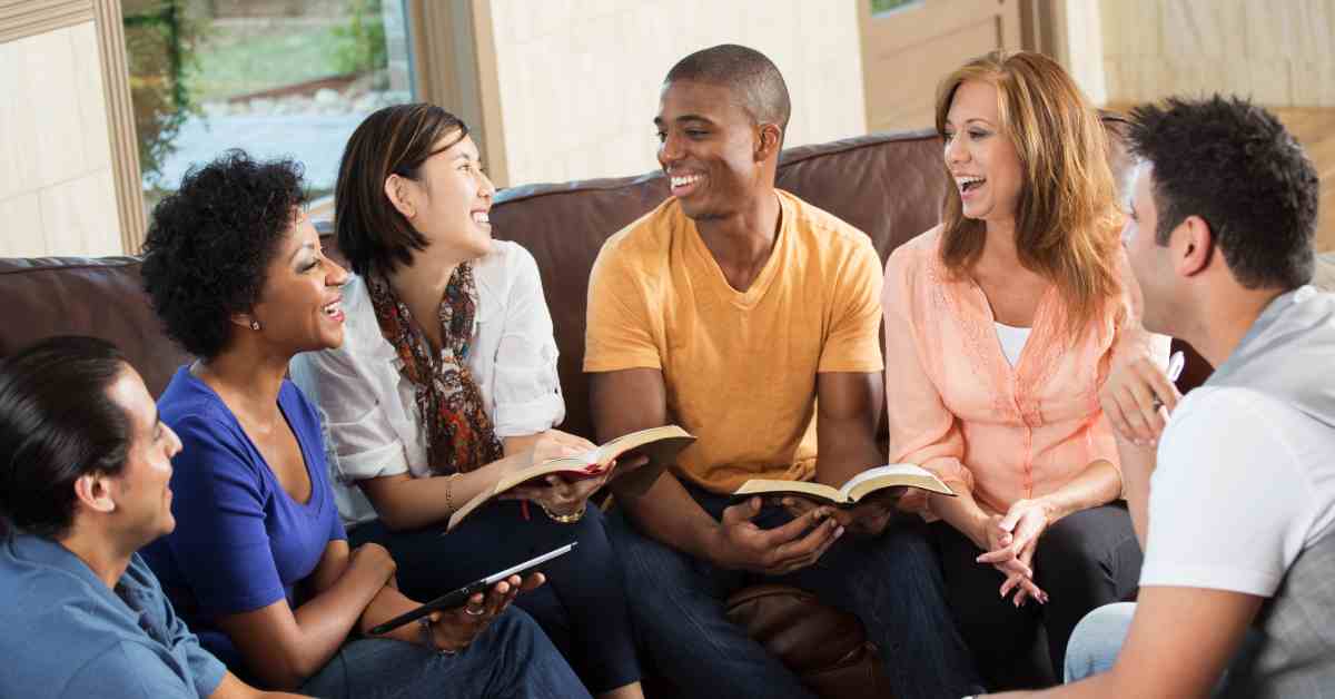 Six adults of different ages and races sitting together with open Bibles and a tablet. They happily converse.